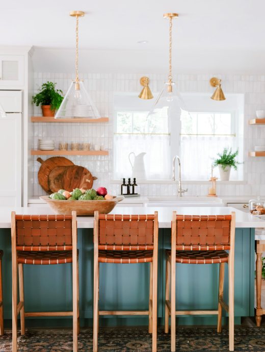 White & teal kitchen island and gold fixtures surrounded by chairs